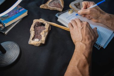 Student taking cataloging note of Red Calcite Geode. clipart