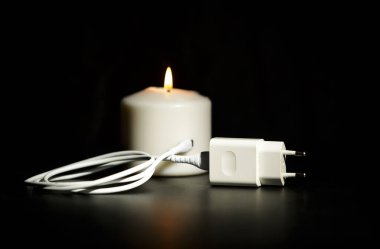 Elektrik kesintisi kavramı. Koyu arka plan aydınlatma mum yakınındaki kablosu ile elektrik şarj cihazı.