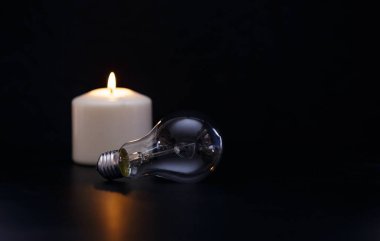 Karanlık bir evde, sönmüş bir ampulün yanında mum yakmak. Elektrik kesintisi, elektrik kesintisi, enerji sızıntısı veya elektrik kesintisi, konsept görüntü.
