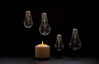 Burning candle near a switched off light bulb in dark home. Blackout, electricity off, load shedding energy crisis or power outage, concept image. clipart