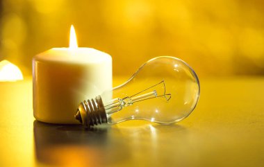 Karanlık bir evde, sönmüş bir ampulün yanında mum yakmak. Elektrik kesintisi, elektrik kesintisi, enerji sızıntısı veya elektrik kesintisi, konsept görüntü.