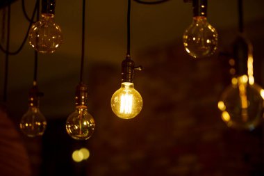 Yanan bir ampul bulanık sarı ışıkların arka planında hafifçe parlar. Enerji krizi. Kesinti.