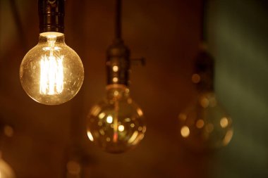 Yanan bir ampul bulanık sarı ışıkların arka planında hafifçe parlar. Enerji krizi. Kesinti.