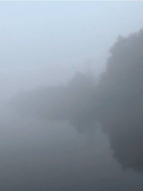 Sis içindeki sakin gölü ile sakin doğal bir manzara, yumuşak gökyüzüne karşı ağaçları yansıtıyor, sakin ve atmosferik bir manzara yaratıyor.