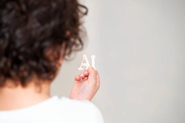 Bir insan elinde ahşap harflerle yapay zeka tutar parmakları pürüzsüz tahtaya dolanır. Mektubun tanecikleri, derileriyle çelişiyor. Kavrayışlarında ince bir sanat eseri oluşturuyor.