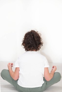 Genç çocuk nilüfer pozisyonunda yerde oturuyor, bacaklarını çapraz yapıyor spor kıyafetleri giyiyor ve rahatlamak için bir tişört giyiyor. Dirsekleri, kalçaları ve dizleri üzerinde hareketlerini çalışırken dinleniyor.