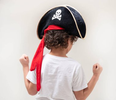 Çocuğun kafatası ve çapraz kemikli bir korsan şapkası var. Kolları kıvrımlı bir tişört ve yakasında beysbol şapkası var.
