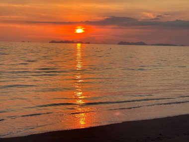 Güneş engin okyanusun üzerinde güzel bir şekilde batıyor ve onun canlı renkleri altındaki sakin suya yansıyor.