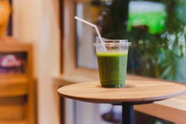 Plastik bardakta yeşil smoothie Kafe 'deki ahşap masada saman