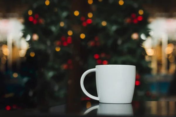 Mug of coffee on table with Christmas light in background