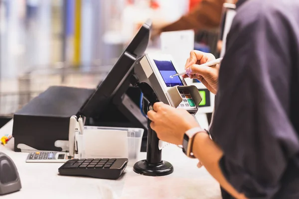 消费者妇女在晚餐市场的信用卡交易机触摸屏上签名 图库图片