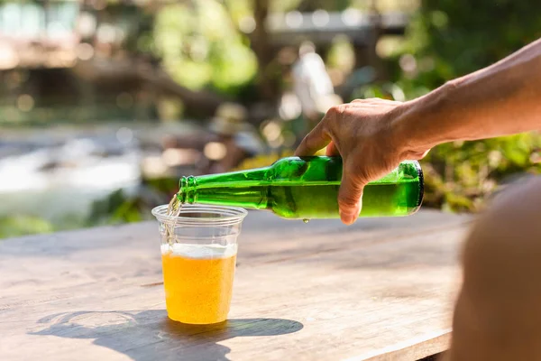 Man pouring beer in plastic glass from bottle during vacation