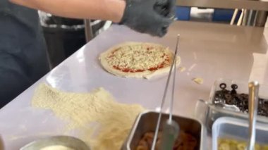 Chef putting black olive and ingredient on pizza.