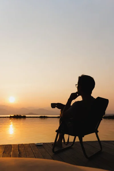 Sylwetka Turysta Siedzieć Krześle Trzymając Filiżankę Kawy Wtaching Wschód Słońca — Zdjęcie stockowe