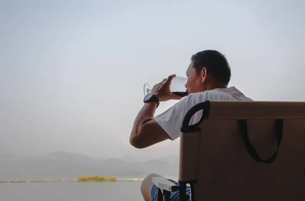 Człowiek Siedzący Krześle Pijący Czerwone Wino Nad Jeziorem — Zdjęcie stockowe