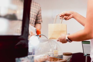 Tezgahtaki garson, paket servis için müşteriye kese kağıdı veriyor.