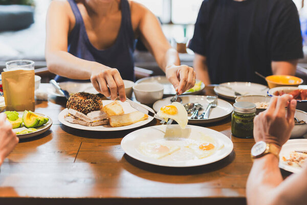 Woman eating fried eggs breakfast with friends on wooden table