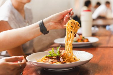 Restoranda arkadaşlarıyla spagetti yiyen bir kadın.