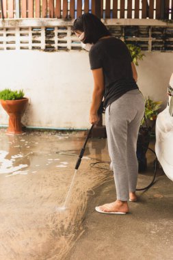 Kadın yüksek basınçlı jetle beton zemini temizliyor.