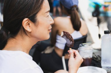 Orta yaşlı bir kadın dondurulmuş muzu çubukta çikolatayla yemekten hoşlanır.