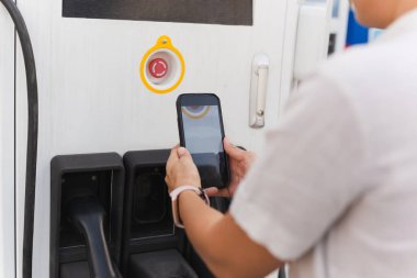 Kadın, kamu elektrik santralinde elektrikli arabayı şarj edecek, ödeme için QR kodunu cep telefonuyla tarayacak.