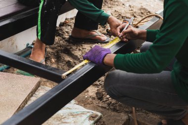 Metal profil uzunluğunu mezura ile ölçen iki kişi