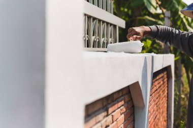 Evin dekorasyonu için dışarıdaki duvarı silindirle boyayan adam.