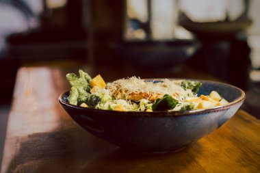 Restoranda tavuklu Sezar salatası ve ahşap tepeli yeşillikler.