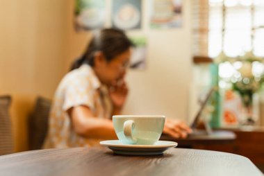 Masada seçilmiş odak kahve fincanı ve arka planda laptopta çalışan bir kadın.