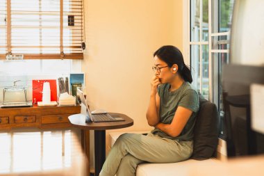 Bilgisayarda çalışan, gözlük takan ciddi bir kadın.