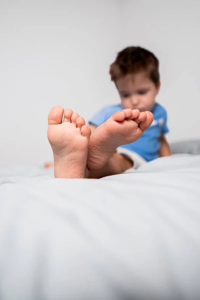 Crossed feet of a child resting peacefully on a bed with light-coloured sheets and a white background.