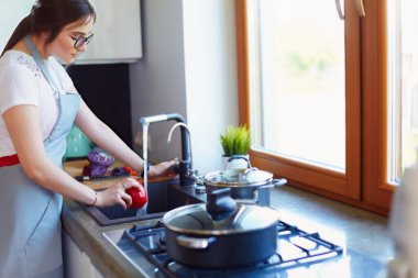 Sebze yıkayan kadın. Güzel genç bir kadın salata için sebze yıkıyor ve mutfakta dururken gülümsüyor..
