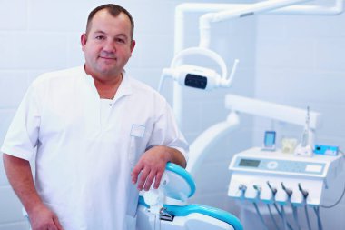 Diş kliniğinde duran gülümseyen bir dişçinin portresi..