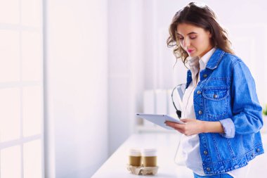 Gülümseyen kadın kahve içiyor ve kafede tablet kullanıyor.