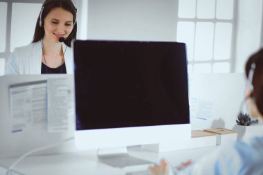 Ofisinde kulaklık ve bilgisayarla gülümseyen iş kadını ya da yardım hattı operatörü.