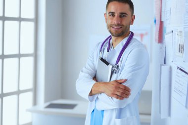 Genç ve kendinden emin erkek doktor portresi tıp ofisinde duruyor.