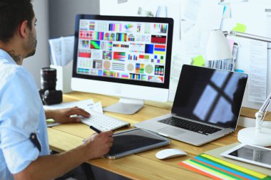 İnternette çalışırken bilgisayarın ve dizüstü bilgisayarın önünde grafik stüdyosunda oturan genç tasarımcının portresi