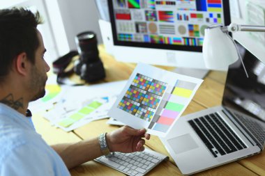 İnternette çalışırken bilgisayarın ve dizüstü bilgisayarın önünde grafik stüdyosunda oturan genç tasarımcının portresi