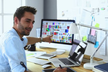 İnternette çalışırken bilgisayarın ve dizüstü bilgisayarın önünde grafik stüdyosunda oturan genç tasarımcının portresi