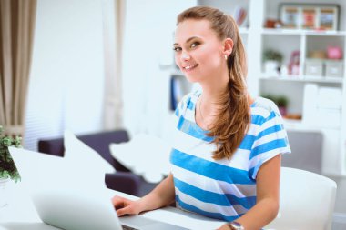 Elinde belgelerle masanın üstünde oturan gülümseyen kadın.