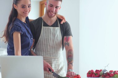 Sebze doğrayan genç bir adam ve mutfakta dizüstü bilgisayarı olan bir kadın..