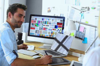 İnternette çalışırken bilgisayarın ve dizüstü bilgisayarın önünde grafik stüdyosunda oturan genç tasarımcının portresi