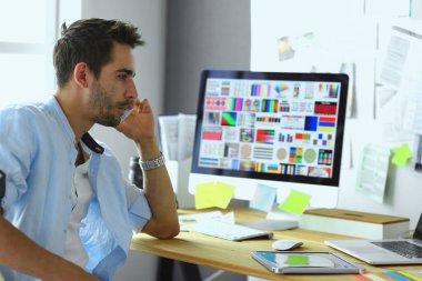 İnternette çalışırken bilgisayarın ve dizüstü bilgisayarın önünde grafik stüdyosunda oturan genç tasarımcının portresi