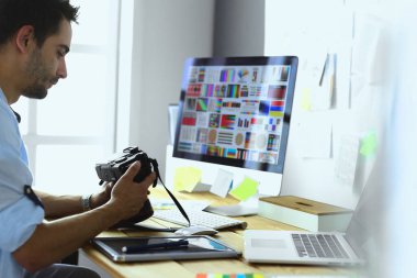 İnternette çalışırken bilgisayarın ve dizüstü bilgisayarın önünde grafik stüdyosunda oturan genç tasarımcının portresi