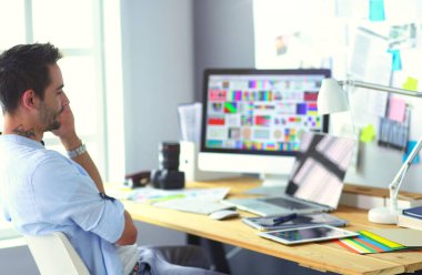 İnternette çalışırken bilgisayarın ve dizüstü bilgisayarın önünde grafik stüdyosunda oturan genç tasarımcının portresi