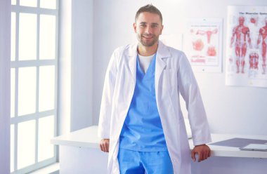 Yakışıklı doktor genç bayan hastasıyla konuşuyor ve ofisinde otururken notlar alıyor.