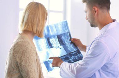 Yakışıklı doktor genç bayan hastasıyla konuşuyor ve ofisinde otururken notlar alıyor.