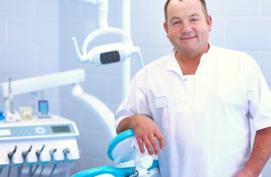 Diş kliniğinde duran gülümseyen bir dişçinin portresi..