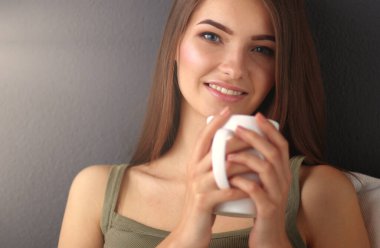 Bir fincan çay ya da kahveyle yerde oturmuş gülümseyen sağlıklı bir genç..