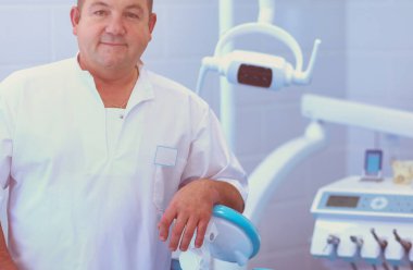 Diş kliniğinde duran gülümseyen bir dişçinin portresi..